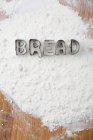 Cookie cutters spelling bread in flour — Stock Photo