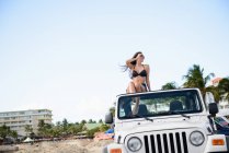 Femme assise sur le toit de la jeep sur la plage — Photo de stock