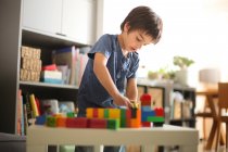Мальчик дома смотрит вниз, играя с красочными кирпичами — стоковое фото