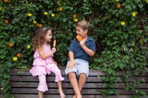 Brother and sister eating ice lollies by plants — Stock Photo