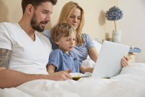 Mãe e pai na cama com filho usando tablet digital — Fotografia de Stock