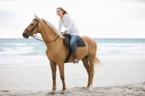 Mujer montando un caballo en la playa - foto de stock