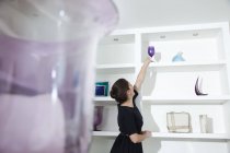 Young woman reaching for wine glass on shelf in living room — Stock Photo