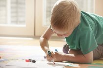 Хлопчик на колінах на підлозі малює на папері — стокове фото
