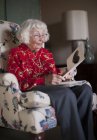 Пожилая женщина сидит в кресле, глядя на поздравительную открытку — стоковое фото