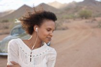 Jovem mulher usando fones de ouvido no deserto em viagem de carro, sorrindo — Fotografia de Stock