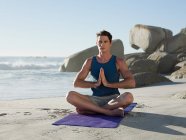 Jeune homme faisant du yoga sur la plage — Photo de stock