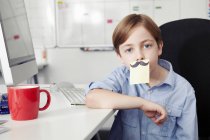 Boy with adhesive note covering mouth, drawing of moustache — Stock Photo