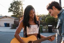 Jeune couple à l'extérieur, jeune femme jouant de la guitare — Photo de stock