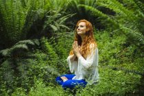 Young woman in forest practicing yoga in lotus position — Stock Photo