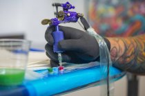 Close up de tatuagem mão mergulhando agulha da arma de tatuagem em tinta vermelha — Fotografia de Stock