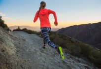 Rear view of young woman trail running on dirt track at dusk on Pacific Crest Trail, Pine Valley, California, USA — Stock Photo
