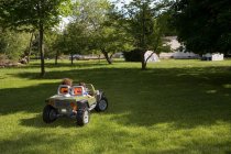 Двое детей за рулем игрушечной машины в саду — стоковое фото