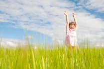 Girl in field with arms raised — Stock Photo