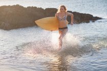 Jeune femme courant en mer avec planche de surf — Photo de stock