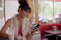 Молода жінка дивиться на мобільний телефон в їдальні — стокове фото