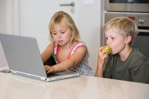 Um irmão e uma irmã usando um laptop — Fotografia de Stock