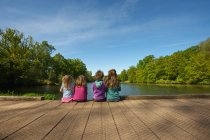 Children sitting on wooden dock in lake — Stock Photo