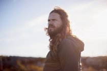 Retrato de homem com cabelos longos em pé contra a paisagem turva — Fotografia de Stock