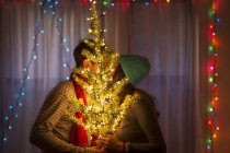 Молодая пара целуется за подсвеченной рождественской елкой — стоковое фото