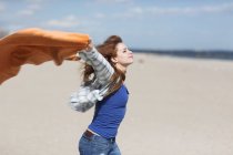 Young woman holding up blanket on windy beach — Stock Photo