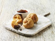 Profiteroles with hot chocolate sauce on wooden board — Stock Photo