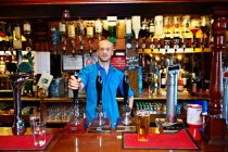 Barman in piedi dietro il bancone del pub — Foto stock