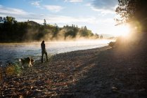 Frau läuft Hund am Ufer des Bitterroot River, Missoula, Montana, USA — Stockfoto