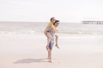 Couple passer un bon moment à la plage avec femme sur les épaules masculines — Photo de stock