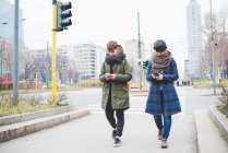 Two sisters walking along street, using smartphones — Stock Photo