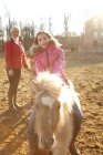 Young girl riding pony, mother watching from behind — Stock Photo