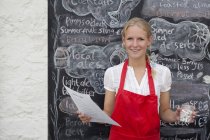 Waitress holding jar of chalk and menu in cafe — Stock Photo