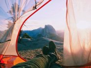 Пара ног торчащих из палатки, горы на заднем плане, Национальный парк Йосемити, Калифорния, США — стоковое фото