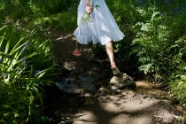 Frau mit Wildblumenstrauß springt über Bach — Stockfoto