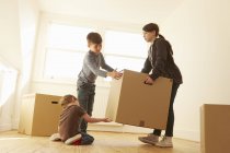 Девушка и два брата поднимают картонную коробку в новом доме — стоковое фото