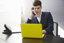 Man sitting at desk using laptop making telephone call — Stock Photo