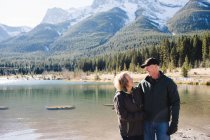Senior couple standing beside river, Three Sisters, Rocky Mountains, Canmore, Alberta, Canada — Stock Photo
