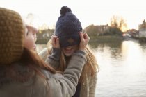 Young woman putting knitted hat on friend — Stock Photo