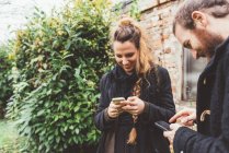 Couple in garden looking at smartphones — Stock Photo