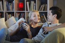 Young couple sitting on sofa with hot drinks — Stock Photo