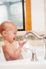 Menina bebê brincando com água na torneira — Fotografia de Stock