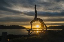 Woman practising yoga by lake at sunset — Stock Photo