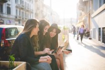 Three young women using digital tablet on city street — Stock Photo