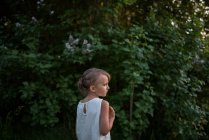 Little girl in green bushes in background — Stock Photo