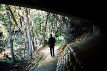 A man in a black jacket and a backpack walks along the path in the forest — Stock Photo