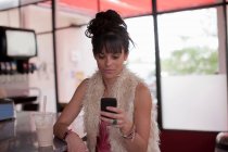 Jovem mulher olhando para o telefone celular no restaurante — Fotografia de Stock