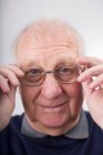 Portrait of senior man adjusting glasses, studio shot — Stock Photo