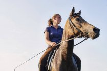 Visão de baixo ângulo da mulher montando cavalo baía contra o céu azul — Fotografia de Stock