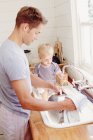 Отец моет посуду, а ребенок играет с водой — стоковое фото