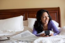 Зріла жінка лежить на ліжку тримає мобільний телефон, посміхаючись — стокове фото
